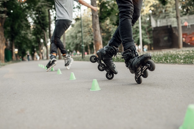 Patinaje sobre ruedas, dos patinador rodando alrededor de los conos en el parque. Patinaje sobre ruedas urbano, deporte extremo activo al aire libre, ocio juvenil, patinaje sobre ruedas