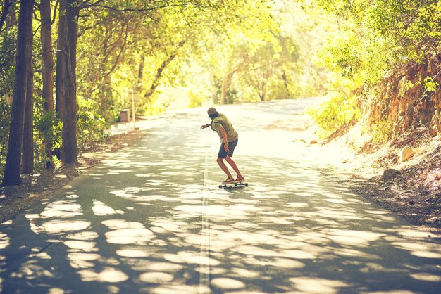 Patinar es sentir la brisa fresca de la libertad Vista trasera de un joven haciendo longboard en la calle