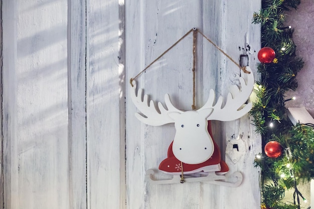 Patines de alces de juguete de madera con un disfraz de Papá Noel colgado en una pared rodeada de ramas de abeto