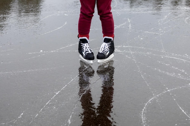 Patines negros sobre hielo Las piernas de las mujeres en pantalones burdeos se paran en la superficie de un lago forestal congelado