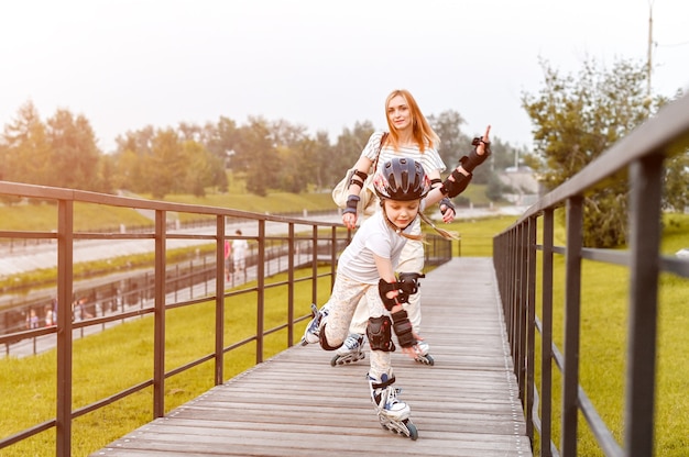 Foto patins de família feliz jovem no parque. caminhada ativa. menina pré-escolar tendo caminhada ativa com a mãe. foco dinâmico