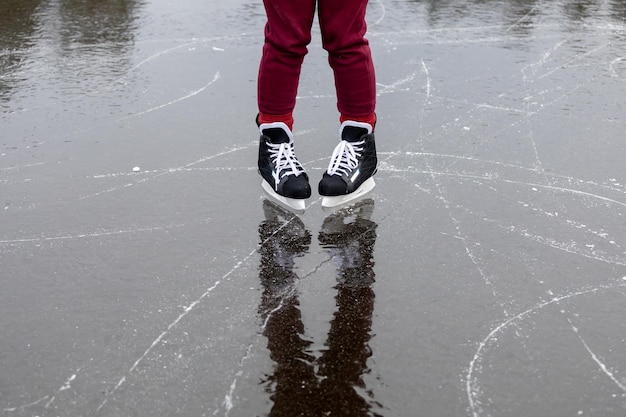 Patins pretos no gelo As pernas das mulheres em calças cor de vinho ficam na superfície de um lago florestal congelado