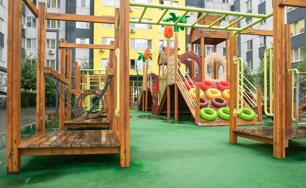 Un patio de edificios de gran altura con un moderno y amplio parque infantil de madera y plástico en un día lluvioso de verano sin gente. Patio al aire libre vacío. Un lugar para juegos y deportes infantiles.