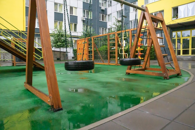 Un patio de edificios de gran altura con un moderno y amplio parque infantil de madera y plástico en un día lluvioso de verano sin gente. Patio al aire libre vacío. Un lugar para juegos y deportes infantiles.