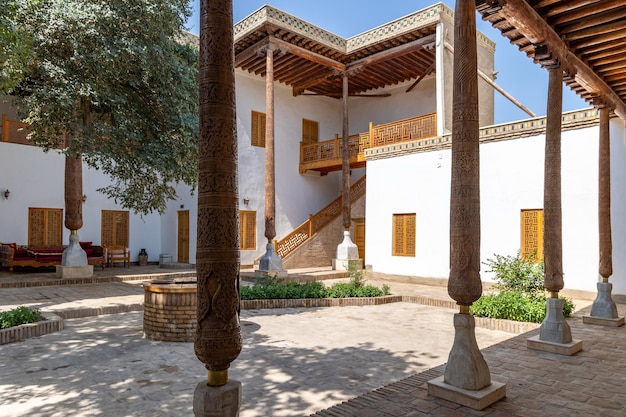 Patio del palacio Nurullaboy saroyi con columnas de madera tallada y paredes blancas Khiva Uzbekistán