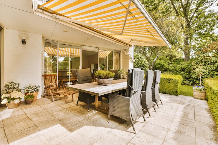 Foto un patio con un paraguas sobre la mesa de comedor y sillas frente a una pared de ladrillo blanco que tiene rayas amarillas en él