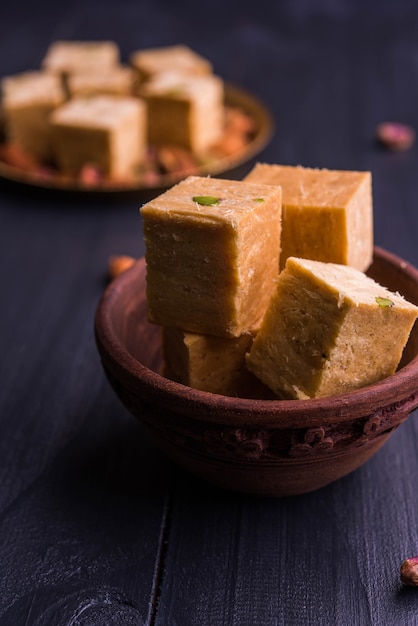 Patisa o Soan Papdi es un popular postre indio en forma de cubo, escamoso y crujiente. Servido con almendras y pistacho en un plato sobre fondo malhumorado. Enfoque selectivo