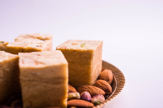 Patisa oder Soan Papdi ist ein beliebtes indisches flockiges und knuspriges Dessert in Würfelform. Serviert mit Mandeln und Pistazien in einem Teller über stimmungsvollem Hintergrund. Selektiver Fokus