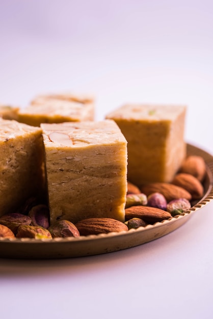 Patisa oder Soan Papdi ist ein beliebtes indisches flockiges und knuspriges Dessert in Würfelform. Serviert mit Mandeln und Pistazien in einem Teller über stimmungsvollem Hintergrund. Selektiver Fokus