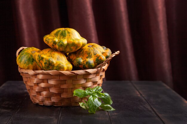 Patissons amarelos ou abóbora em uma cesta de vime e uma folha de manjericão em um fundo de madeira marrom.