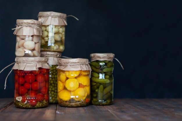 Foto patissons en escabeche, pepinos, champiñones, guisantes verdes y tomates enlatados en frascos de vidrio