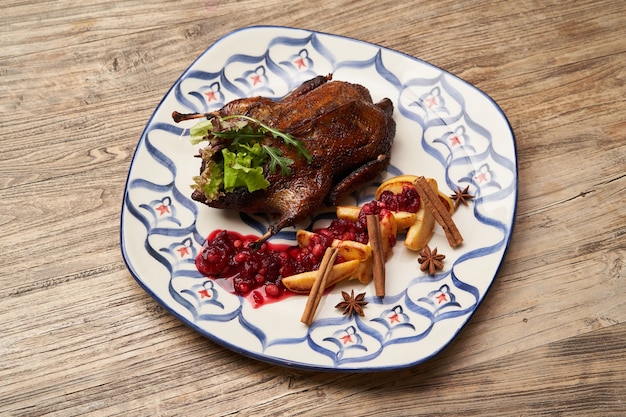 Pato asado con membrillo sobre fondo de mesa de madera. Pato entero al horno con salsa de membrillo y frutos rojos.