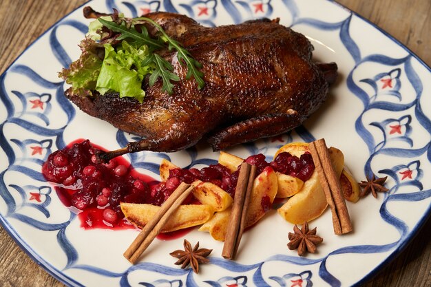 Pato asado con membrillo sobre fondo de mesa de madera. Pato entero al horno con salsa de membrillo y frutos rojos.