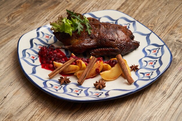 Pato asado con membrillo sobre fondo de mesa de madera. Pato entero al horno con salsa de membrillo y frutos rojos.