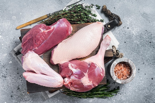 Pato entero descuartizado, pechuga cruda, patas de bistec, alas en una tabla de cortar de carnicero, fondo gris, vista superior