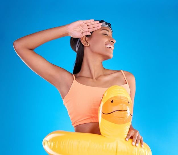 El pato de goma sonríe y saluda con una mujer nadadora en el estudio sobre fondo azul con gafas de protección en la cabeza Gesto de mano feliz y nadando con una atractiva hembra joven emocionada de nadar en verano