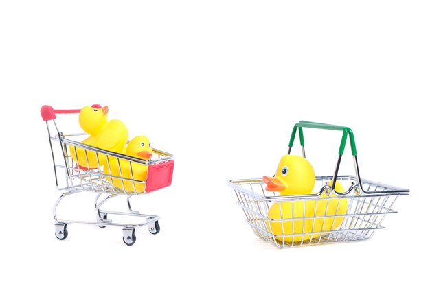 Patos de goma amarillos en el carrito de compras sobre un fondo blanco. Bienes y compras para niños.