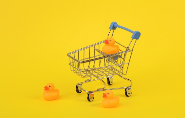 Patos de goma con carrito de compras en fondo amarillo Diseño creativo de Ninimalismo