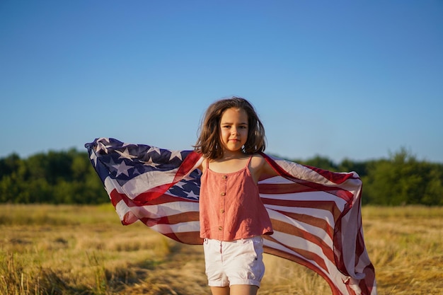 Patriota de garotinha feliz correndo no campo com bandeira americana