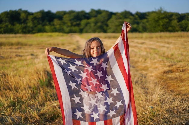 Patriota de garotinha feliz correndo no campo com bandeira americana