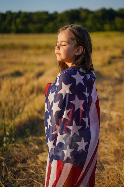 Patriota niña feliz corriendo en el campo con bandera americana.