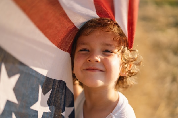 Patriota niño feliz corriendo en el campo con bandera americana. Estados Unidos celebra el 4 de julio