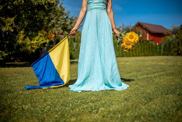 Patriotische Frau in blauem Kleid mit ukrainischer Flagge und Sonnenblumen, die sich für den Frieden einsetzt. Stoppt den Krieg