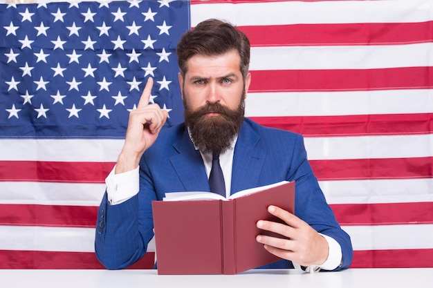 Patriotisches Konzept Amerikanischer Anwaltslehrer oder Fernsehmoderator halten Buch Hintergrund der amerikanischen Flagge Liebe Heimat Mann mit Bart und Schnurrbart ernstes Gesicht mit amerikanischer Flagge Machen Sie Amerika wieder großartig