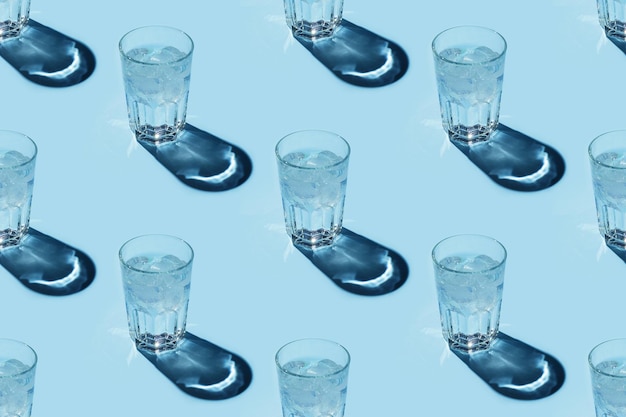 Patrón sin costuras con vasos transparentes de agua con hielo sobre fondo azul