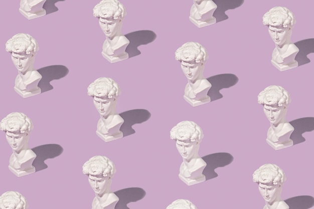 Patrón de fondo de bustos griegos o romanos blancos dispuestos en líneas de color púrpura pastel con sombras laterales en una vista de ángulo alto