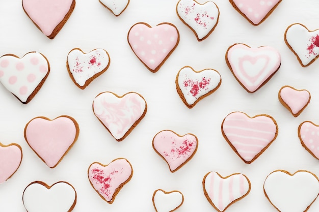 Patrón de galletas de jengibre en forma de corazón decorado con esmalte blanco y rosa sobre una superficie de madera blanca