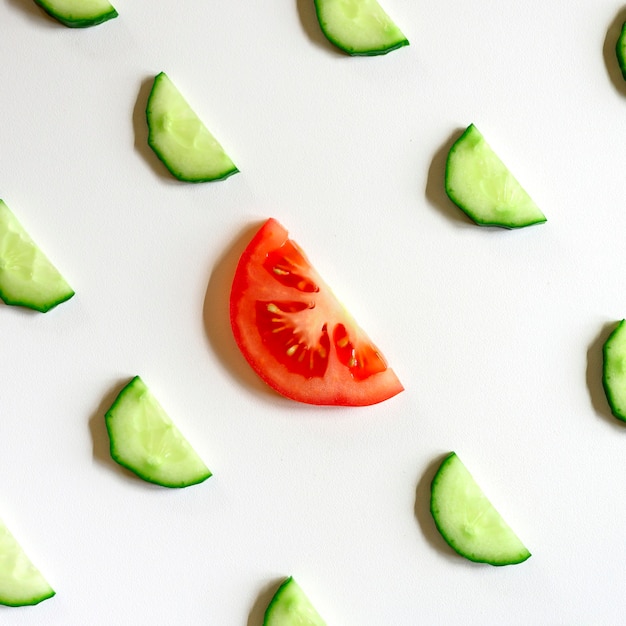 Patrón repetitivo de semicírculos en rodajas de pepinos vegetales crudos frescos para ensalada y una rodaja de tomate en el centro aislado en un fondo blanco plano, vista superior. cuadrado