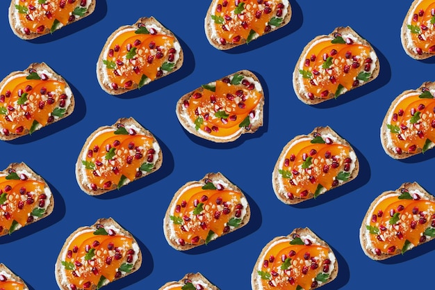 Patrón de tostadas con queso crema, caqui y semillas de granada en fondo azul Concepto de foto de comida creativa vista superior