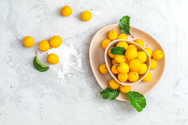 Patrón de verano creativo hecho de ciruelas cerezas amarillas frescas en un tazón rosa sobre fondo de hormigón gris Concepto mínimo de fruta Lay plano