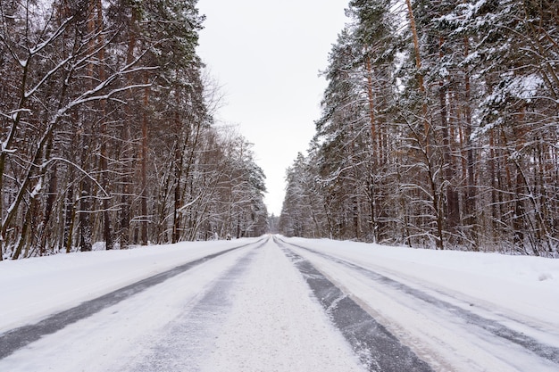 Foto patrones en la carretera de invierno en forma de cuatro líneas rectas. camino nevado en el fondo del bosque nevado. paisaje de invierno.