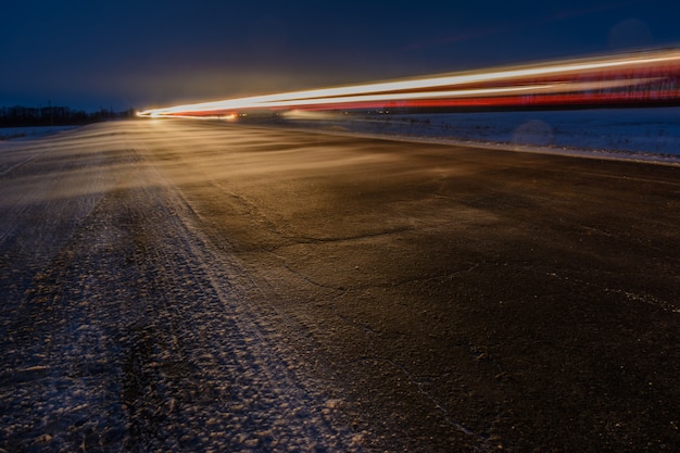 Patrones de los faros de los automóviles en la carretera de invierno de noche en forma de líneas blancas y rojas. Una fuerte tormenta de nieve barre la carretera con nieve. Camino peligroso. Paisaje de invierno.