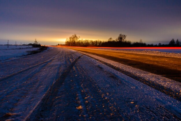 Patrones de los faros de los automóviles en la carretera de invierno de noche en forma de líneas blancas y rojas. Una fuerte tormenta de nieve barre la carretera con nieve. Camino peligroso. Paisaje de invierno.