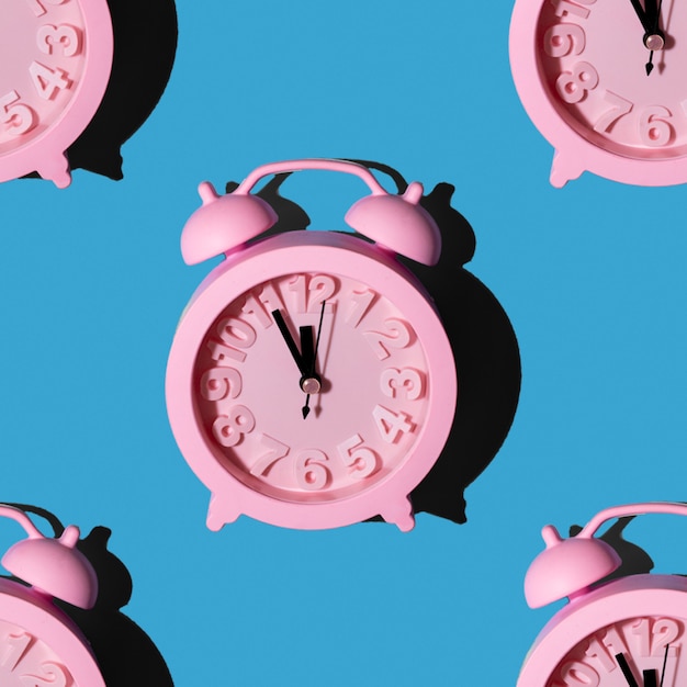 Patrones de moda con relojes de color rosa sobre fondo azul repitiendo papel tapiz con diseño minimalista sin costuras. Año nuevo en concepto de medianoche