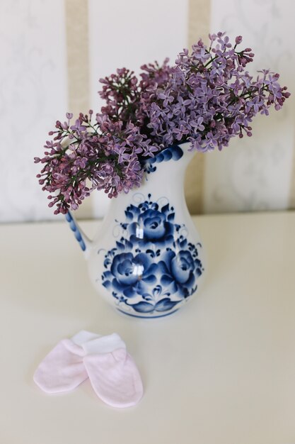 patucos de bebé y ropa con un ramo de flores lilas en el fondo