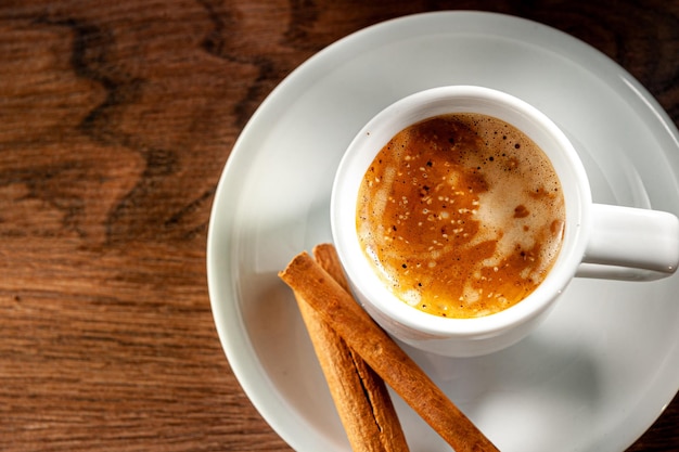 Paus de canela e café expresso em um copo curto sobre fundo de madeira