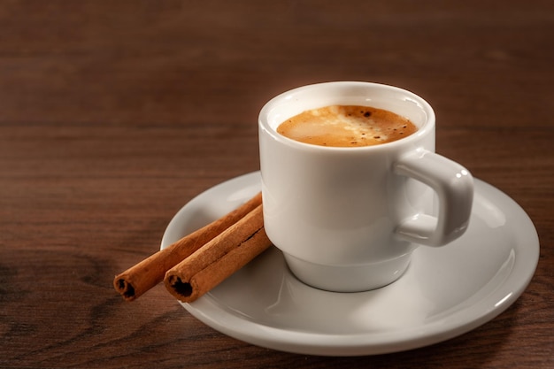 Foto paus de canela e café expresso em um copo curto sobre fundo de madeira