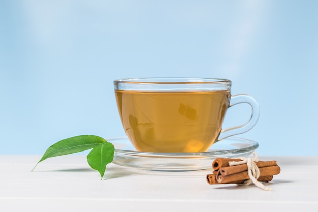 Paus de canela e chá com folhas verdes em uma mesa branca sobre um fundo azul. Uma bebida revigorante útil para a saúde.