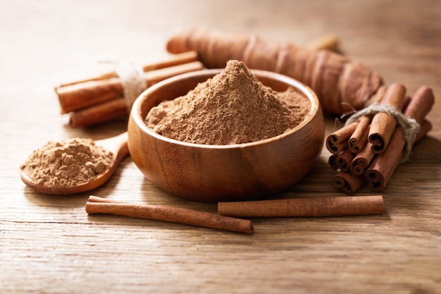 Paus de canela e tigela de canela em pó em uma mesa de madeira