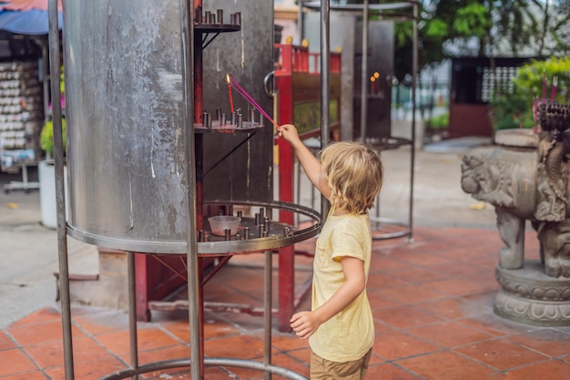 Paus de incenso na panela de incenso estão queimando e usam fumaça para prestar respeito ao Buda, incensos na mão do menino e uso de fumaça para orar em respeito ao Buda na vida do budismo