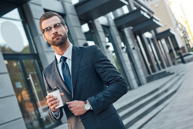 Pausa para el café rápido apuesto joven en traje completo y glas