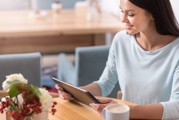 Pausa para el café relajante. Atractiva mujer joven feliz relajarse y leer mientras usa su gadget en una cafetería.