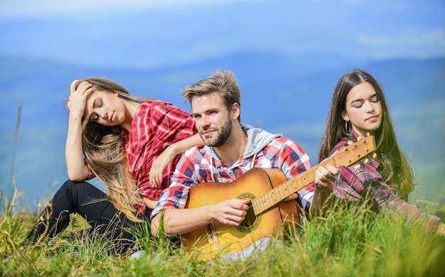 Pausa musical. Entretenimiento de senderismo. Lugar pacífico. Melodía de la naturaleza. Tradición senderista. Amigos caminando con música. Gente descansando en la cima de la montaña mientras un hombre guapo tocando la guitarra. Cantando juntos.