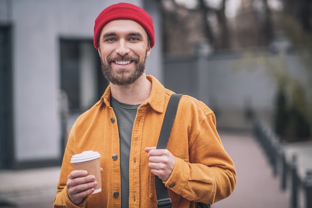 Pausa para o café. Homem com chapéu vermelho e jaqueta laranja com uma xícara de café nas mãos