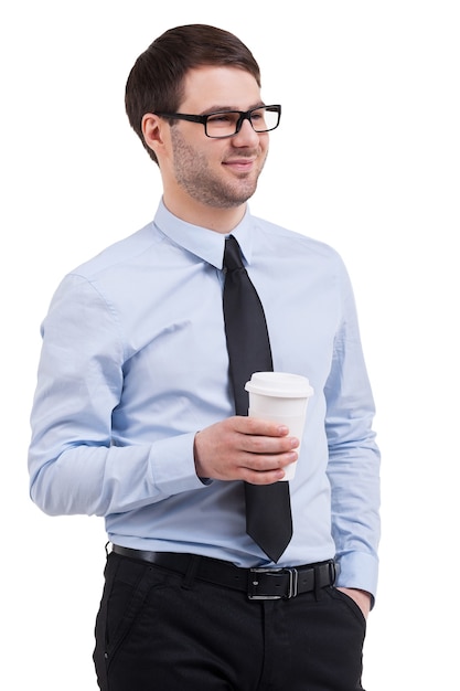 Pausa para o café. Jovem confiante de camisa e gravata, segurando uma xícara de café e olhando para longe em pé isolado no branco