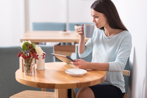 Pausa para o café relaxante. mulher morena bonita alegre sorrindo e lendo enquanto relaxa em um café usando seu gadget.